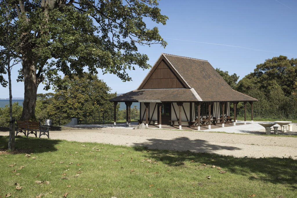 Architectural photograph of the restored 19th-century timber-framed kiosk in Blackrock Park, Dublin, carefully conserved and repurposed as a tearoom with repaired timberwork, new glazing, restored veranda seating, and upgraded landscaping, designed by 7L Architects and built by Bracegrade.